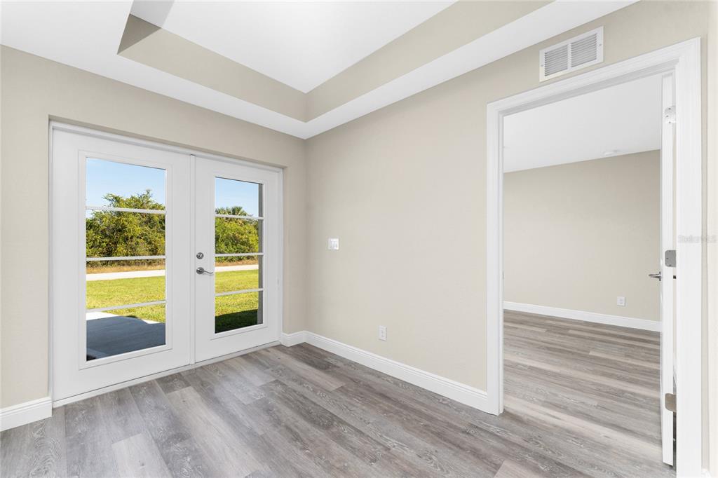 A room with gray wood-look flooring, a tray ceiling, and glass doors leading outside — 6397 FILBERT STREET, NORTH PORT, FL