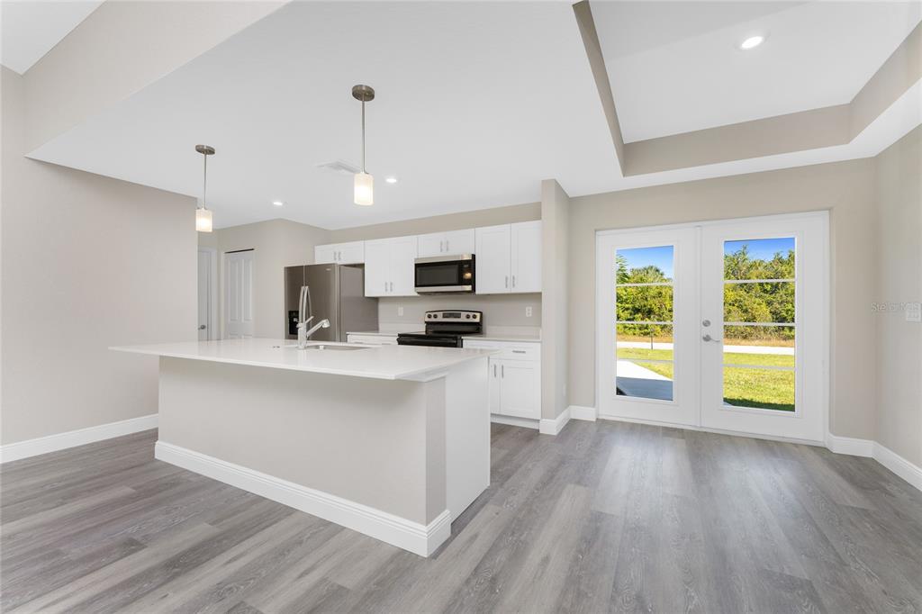 A modern kitchen features white cabinets, a central island, stainless steel appliances, and gray flooring — 6397 FILBERT STREET, NORTH PORT, FL