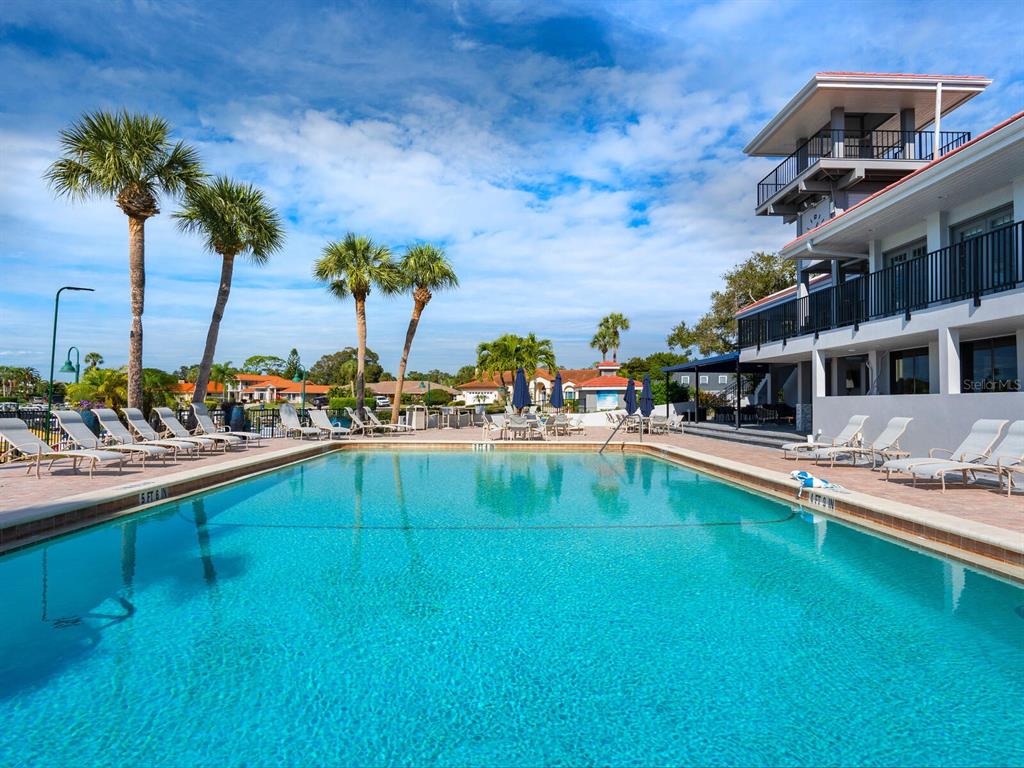 A swimming pool sits in front of a multi-story building with balconies and palm trees — 1355 SOUTHBAY DRIVE, OSPREY, FL
