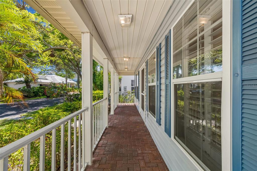 A covered porch with a brick floor, white railings, and blue shutters on the house exterior — 6414 23RD AVE DR W, BRADENTON, FL