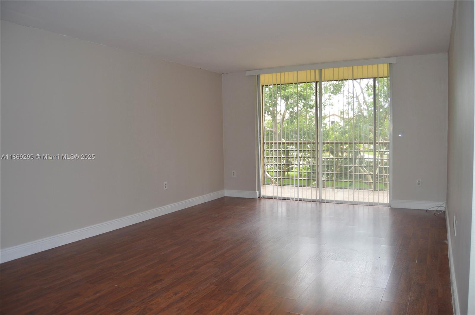 An empty room features wood-look flooring, light-colored walls, and a sliding glass door with blinds — 3490 Foxcroft Rd # B212, Miramar FL 33025, MIRAMAR, FL
