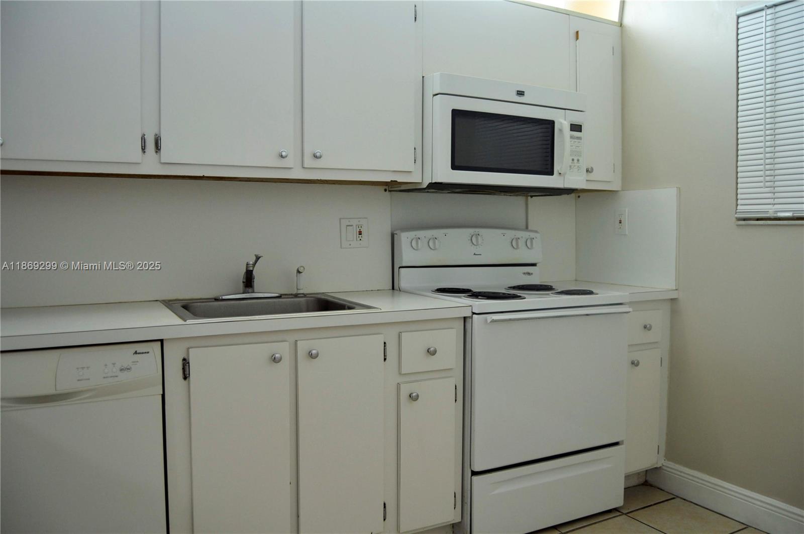 A kitchen features white cabinets, a stainless steel sink, and white appliances — 3490 Foxcroft Rd # B212, Miramar FL 33025, MIRAMAR, FL