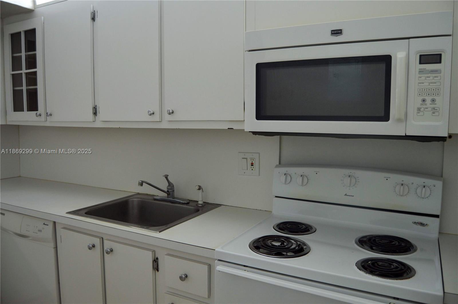 A kitchen features white cabinets, a stainless steel sink, and white appliances — 3490 Foxcroft Rd # B212, Miramar FL 33025, MIRAMAR, FL