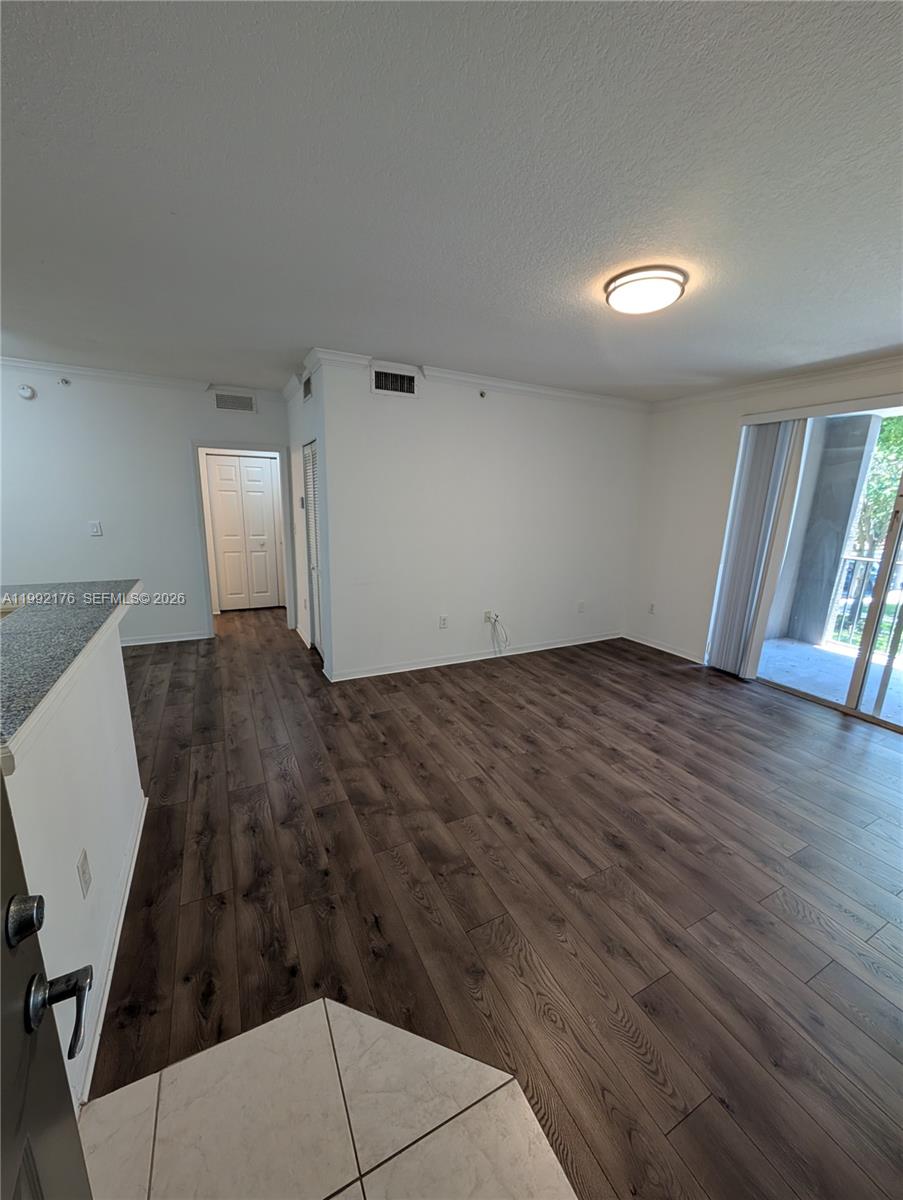 An empty living room features dark wood-look flooring, white walls, and a sliding glass door — 6831 SW 44th St # 203, Miami FL 33155, MIAMI, FL