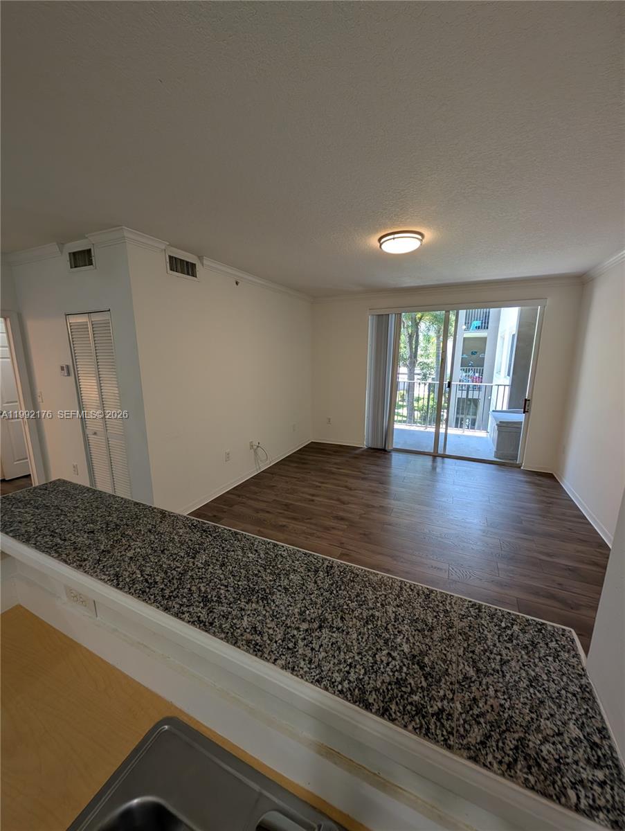 A kitchen counter with a granite top overlooks an empty living area with wood flooring — 6831 SW 44th St # 203, Miami FL 33155, MIAMI, FL