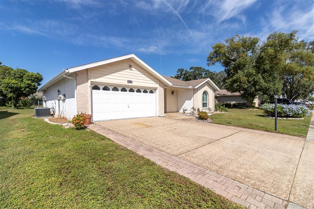 A single-story house with a white garage door, beige siding, and a paved driveway — 4719 CAVENDISH DRIVE, NEW PORT RICHEY, FL