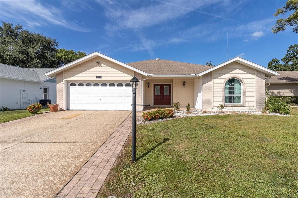 A single-story house with a two-car garage, beige siding, and a front lawn — 4719 CAVENDISH DRIVE, NEW PORT RICHEY, FL