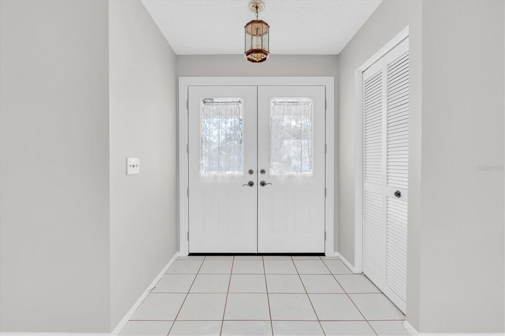 A foyer with white tiled floors, a double front door, and a louvered closet door — 4719 CAVENDISH DRIVE, NEW PORT RICHEY, FL