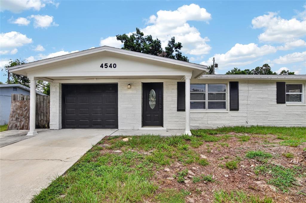 A single-story white brick house features a front-facing garage, a dark door, and black shutters — 4540 IRENE LOOP, NEW PORT RICHEY, FL