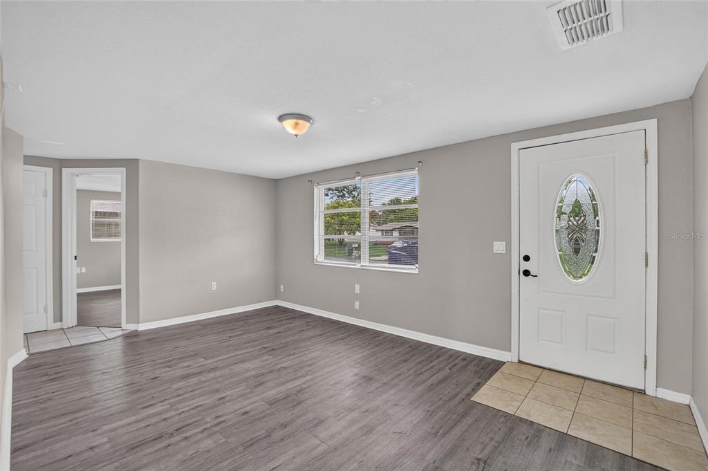 A living room with gray walls, wood-look flooring, a white front door, and a window — 4540 IRENE LOOP, NEW PORT RICHEY, FL