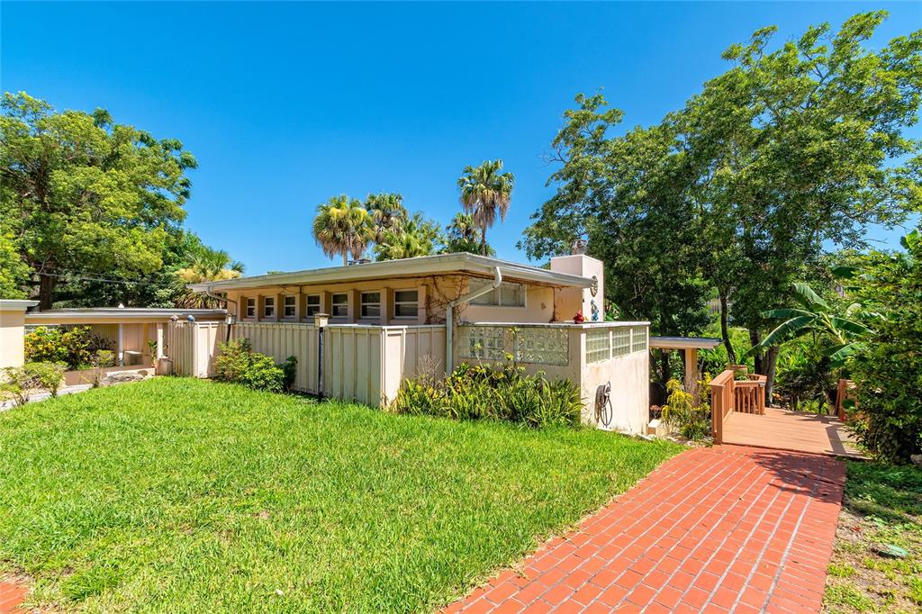A low-slung house with a brick walkway, glass block accents, and mature trees under blue sky — 2425 LAKE SUE DRIVE, ORLANDO, FL