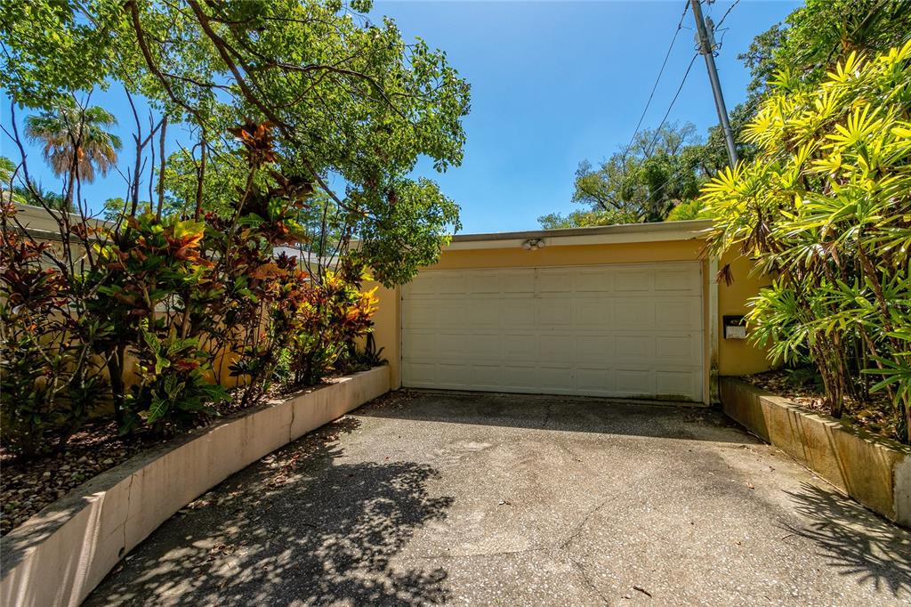 A concrete driveway leads to a single-car garage surrounded by lush tropical landscaping — 2425 LAKE SUE DRIVE, ORLANDO, FL