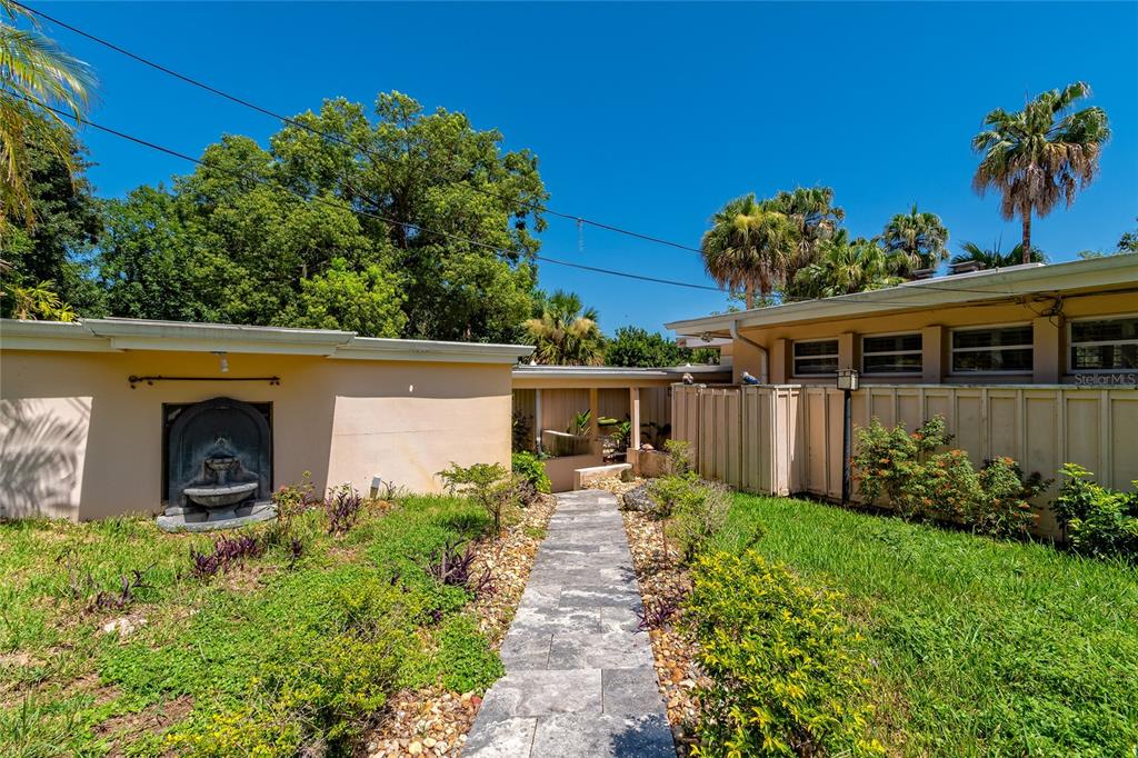 A stone walkway leads between a tan building with a fountain and a fenced structure — 2425 LAKE SUE DRIVE, ORLANDO, FL