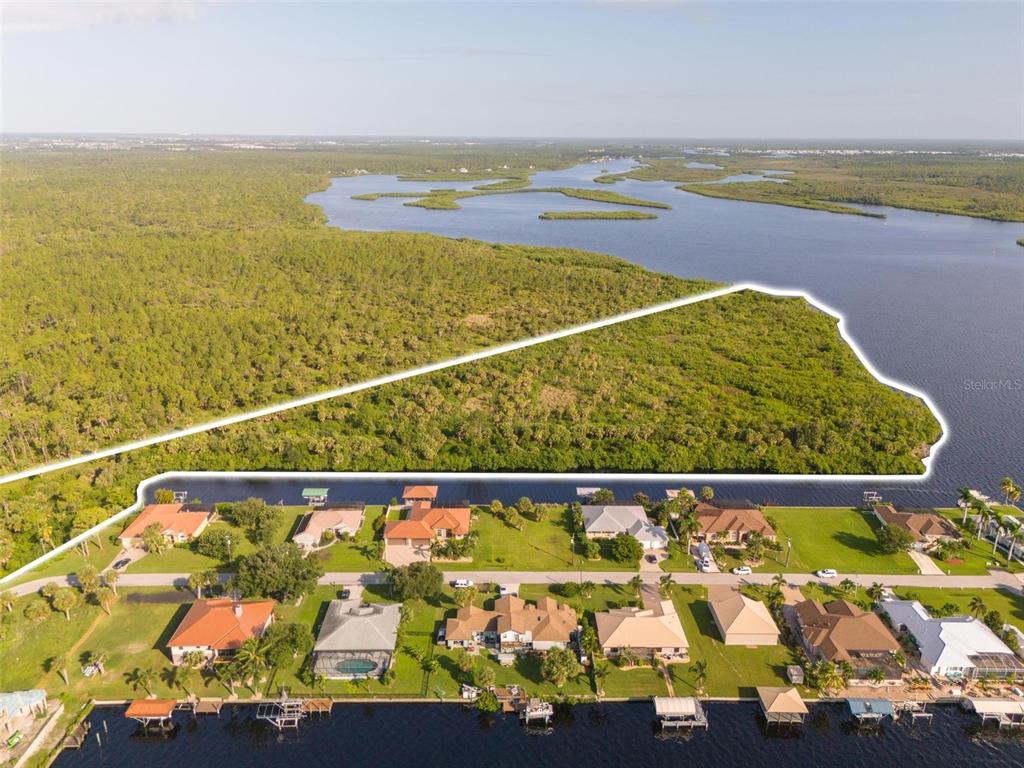An aerial view shows a large, undeveloped waterfront lot outlined in white above residential homes — 2925 VANCE TERRACE, PORT CHARLOTTE, FL