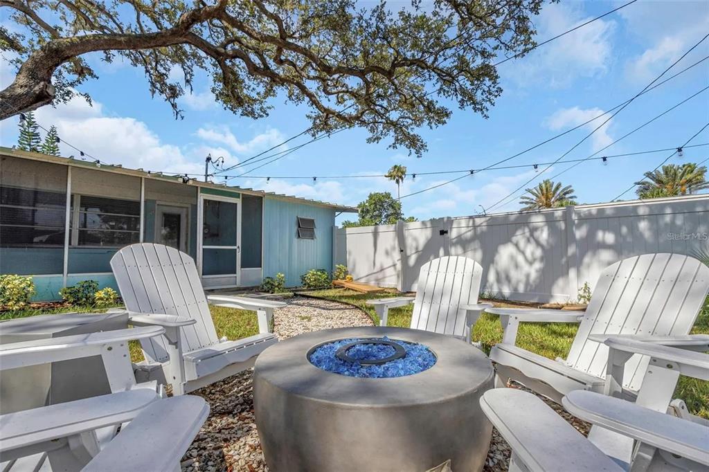 A backyard fire pit area features white Adirondack chairs on a gravel patio — 1500 CLEARWATER LARGO ROAD N, LARGO, FL