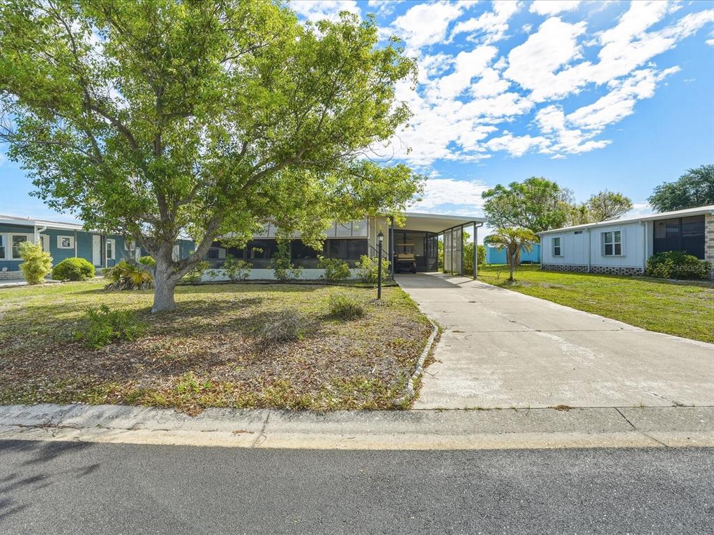 A single-story manufactured home with a concrete driveway and a large tree in front — 6144 REDWING AVENUE, ENGLEWOOD, FL