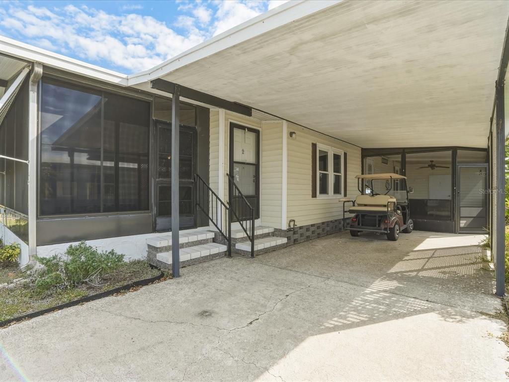 A mobile home exterior features a concrete carport, a golf cart, and two screened porches — 6144 REDWING AVENUE, ENGLEWOOD, FL
