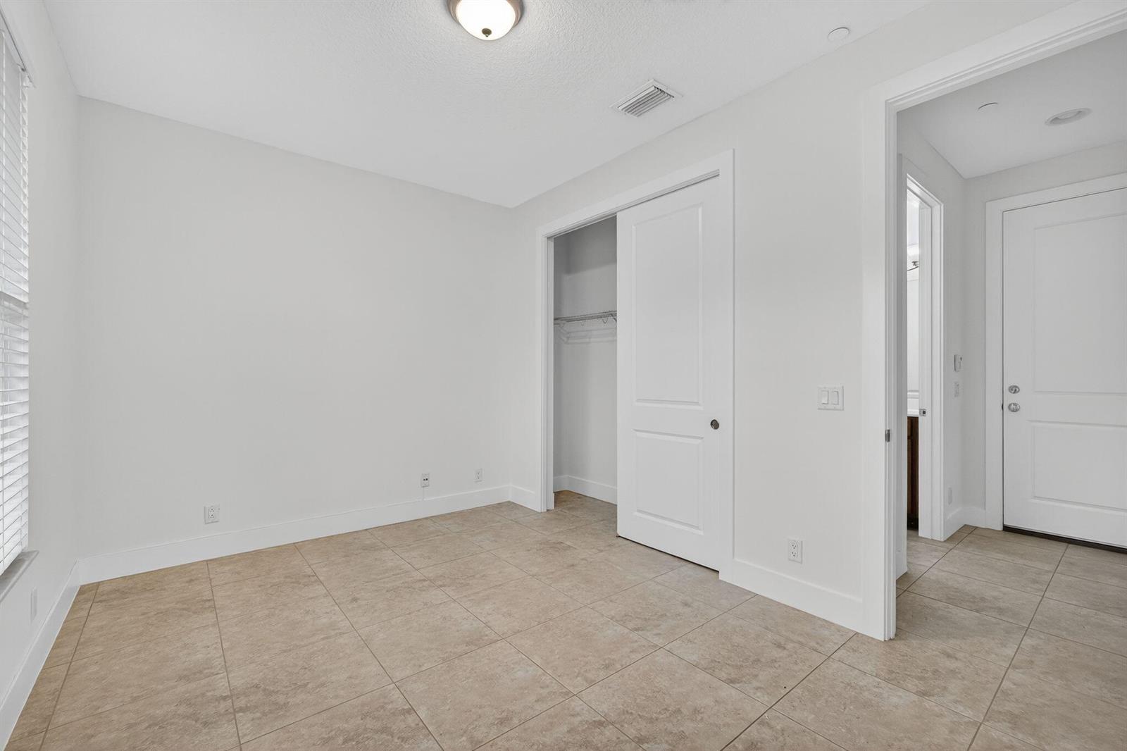 An empty bedroom features white walls, tile flooring, a closet, and a doorway to a bathroom — 7089 Edison Place, Palm Beach Gardens FL 33418, PALM BEACH GARDENS, FL