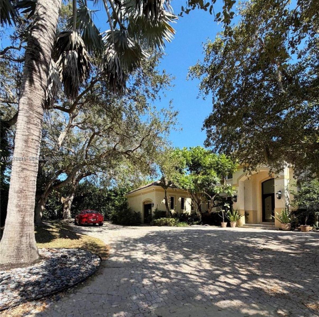 A paved driveway leads to a house entrance surrounded by large trees and a palm — 673 Destacada Ave, Coral Gables FL 33156, CORAL GABLES, FL