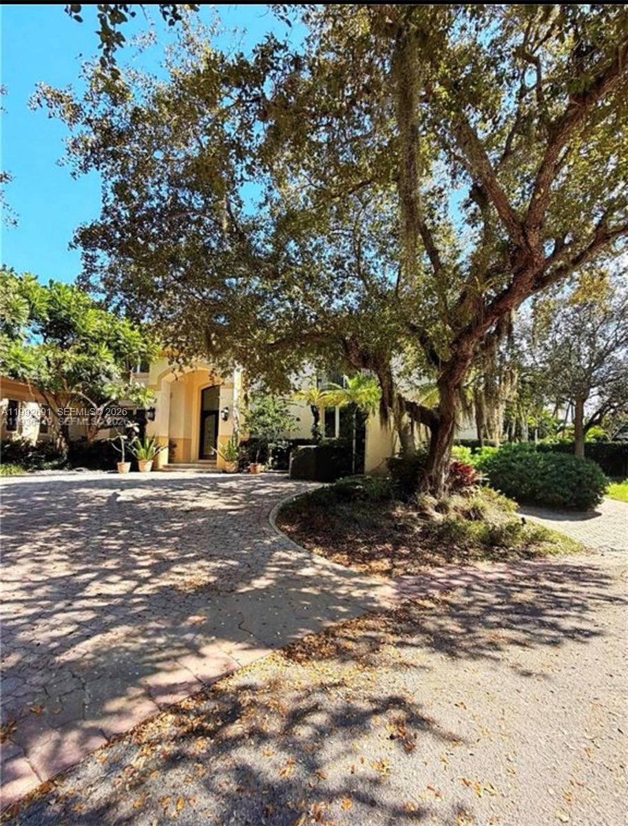 A paved circular driveway leads to the entrance of a house shaded by large trees — 673 Destacada Ave, Coral Gables FL 33156, CORAL GABLES, FL