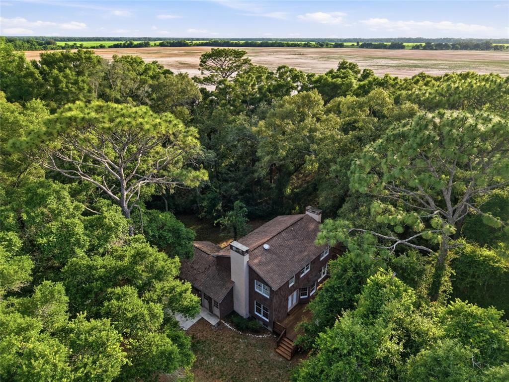 An aerial view shows a two-story brick house nestled within a dense forest — 9291 NW 127TH PLACE, CHIEFLAND, FL