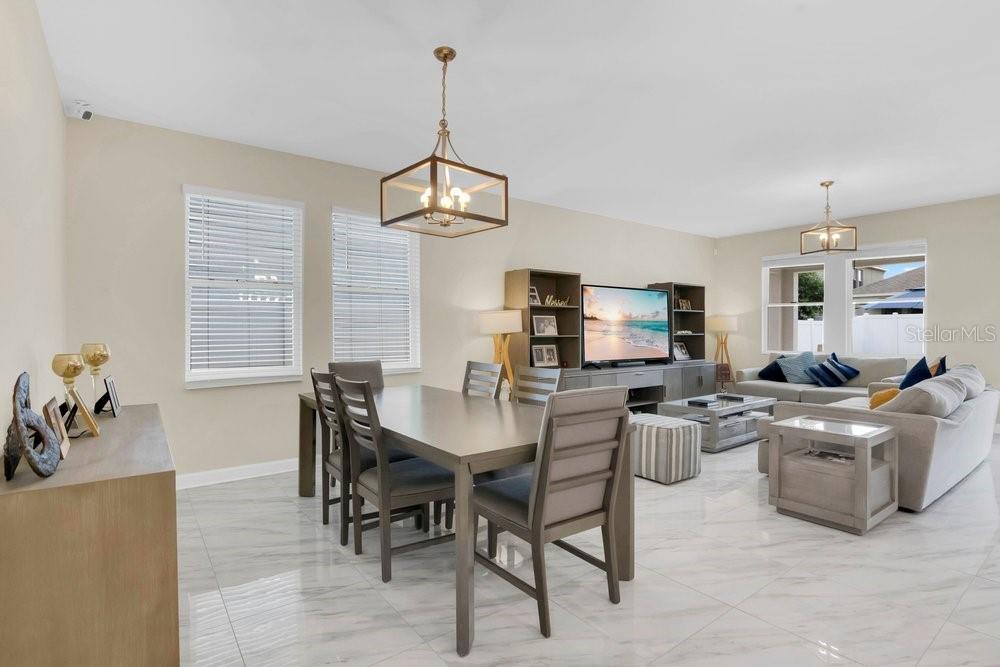 An open-concept living and dining area features light-colored tile flooring and modern light fixtures — 11036 ROBERT FROST DRIVE, WINTER GARDEN, FL