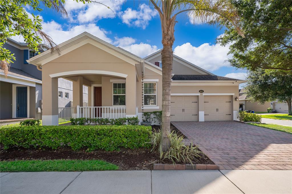 A tan single-story house with a covered front porch, two-car garage, and brick paver driveway — 8031 NAVEL ORANGE LANE, WINTER GARDEN, FL