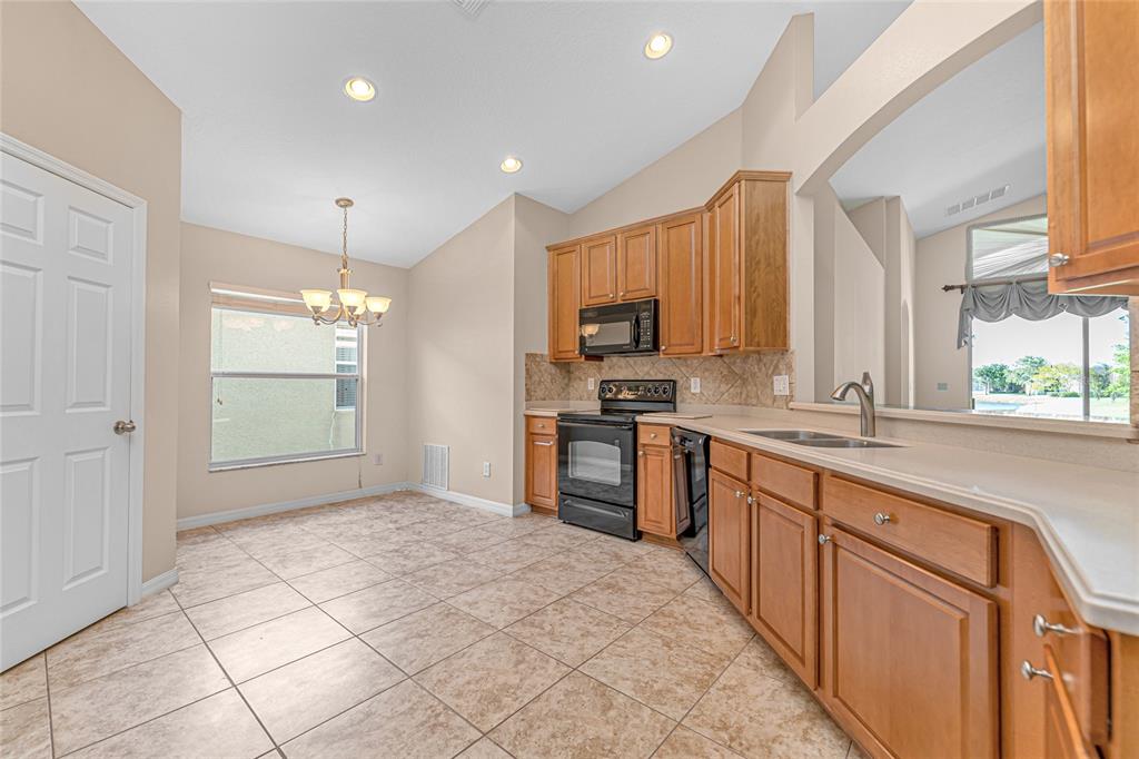 A kitchen with wood cabinets, black appliances, tile flooring, and an adjacent dining area — 14921 BRAYWOOD TRAIL, ORLANDO, FL