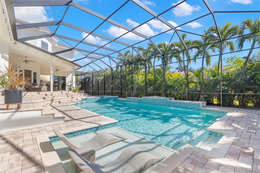 A screened-in swimming pool with a sun shelf and lounge chairs on a paved patio — 5264 61ST AVENUE S, ST PETERSBURG, FL
