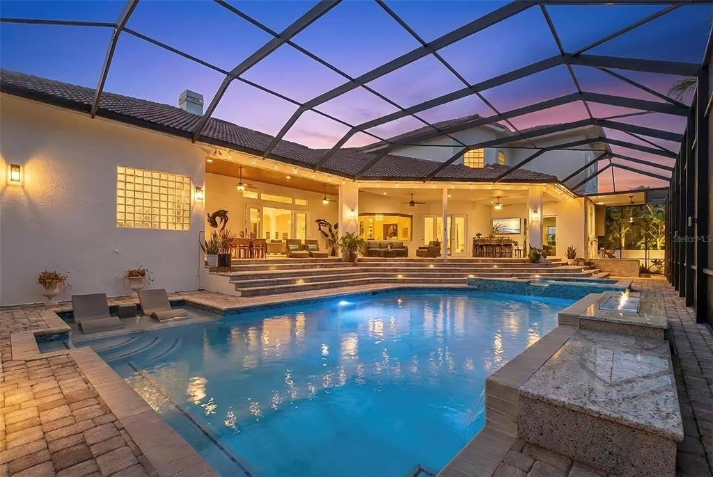 A swimming pool with a sun shelf sits under a screened lanai at dusk — 5264 61ST AVENUE S, ST PETERSBURG, FL