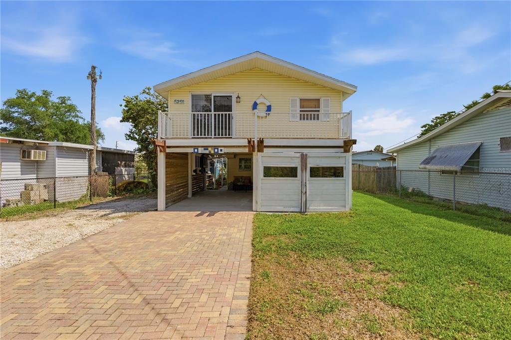 A yellow elevated house features a paved driveway, a lower-level garage, and a front balcony — 5251 ALPACA DRIVE, WEEKI WACHEE, FL