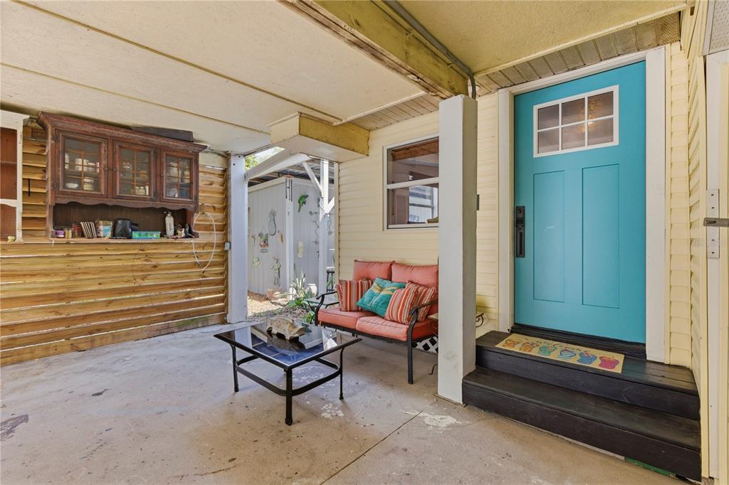 A covered patio features a teal front door, a small sofa, and a glass coffee table — 5251 ALPACA DRIVE, WEEKI WACHEE, FL