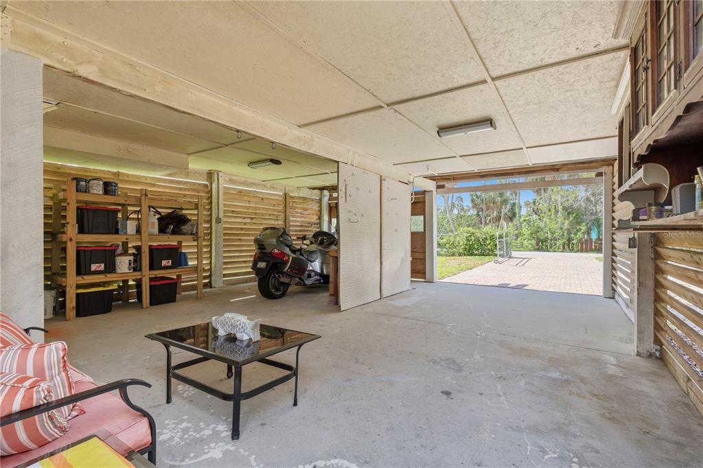 An open-air garage features a concrete floor, wooden slat walls, storage shelving, and a parked motorcycle — 5251 ALPACA DRIVE, WEEKI WACHEE, FL