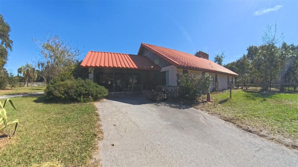 A single-story house with a red tile roof and a screened-in carport sits on grass — 4540 W HIGHWAY 318, CITRA, FL