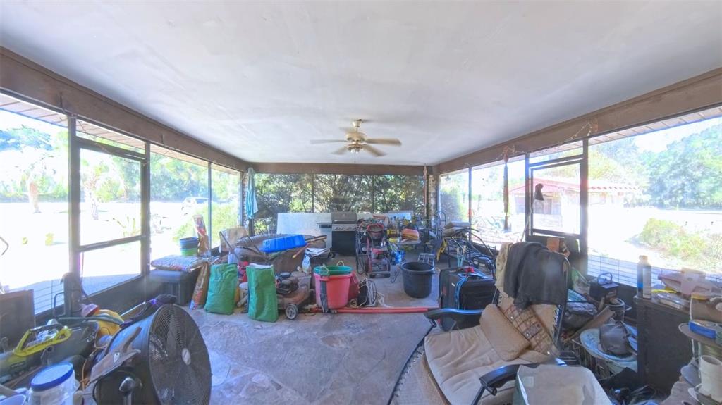 A cluttered screened-in porch features a stone floor, a ceiling fan, and large window screens — 4540 W HIGHWAY 318, CITRA, FL