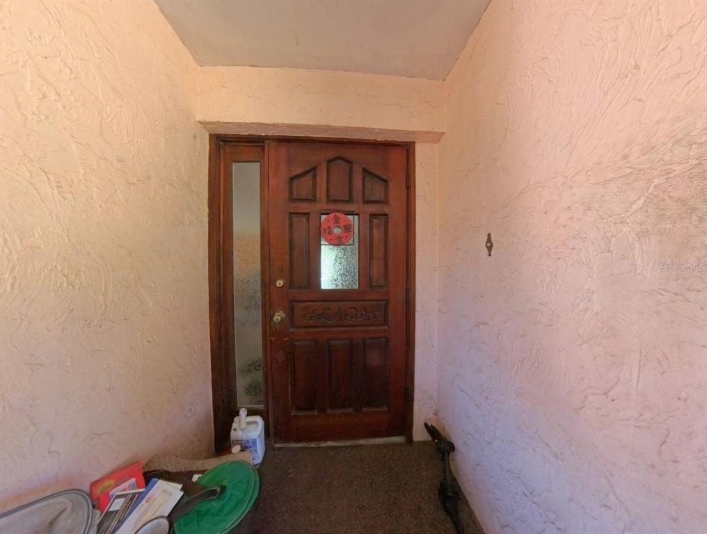 A wooden front door with a glass panel is set within a pink textured entryway — 4540 W HIGHWAY 318, CITRA, FL