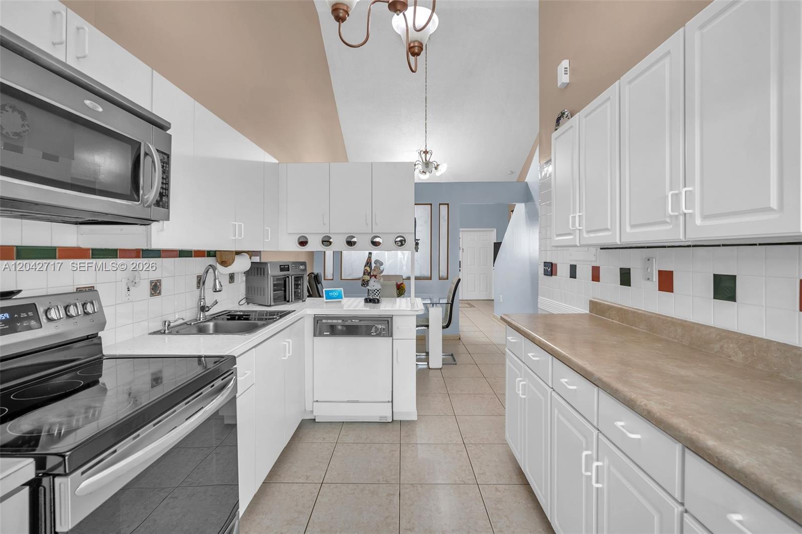 A kitchen features white cabinets, stainless steel appliances, tan countertops, and tiled flooring — 9018 NW 120th St # 133, Hialeah Gardens FL 33018, HIALEAH GARDENS, FL