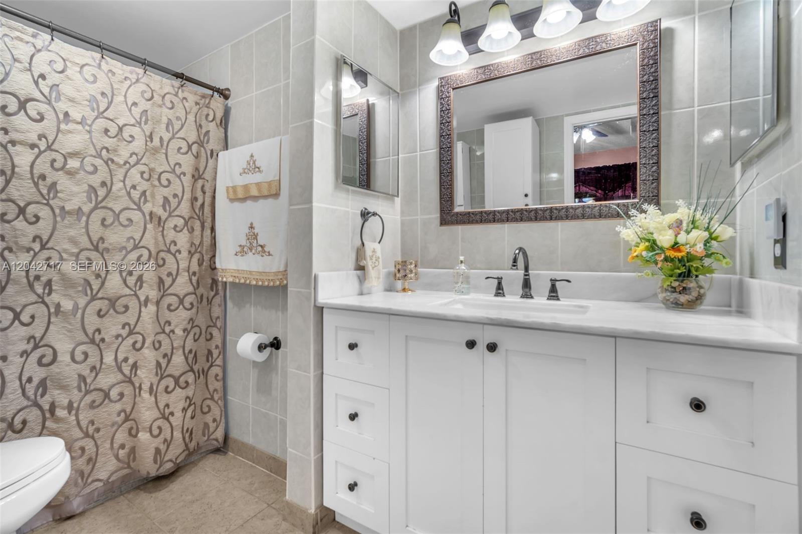 A bathroom features a white vanity with a marble countertop, a framed mirror, and tiled walls — 9018 NW 120th St # 133, Hialeah Gardens FL 33018, HIALEAH GARDENS, FL