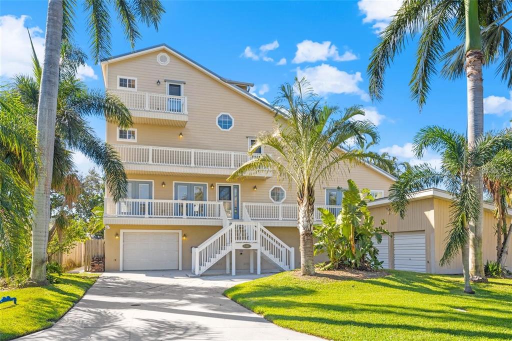 A three-story tan house with multiple balconies, a garage, and palm trees in the yard — 1902 ARROWHEAD DRIVE NE, ST PETERSBURG, FL