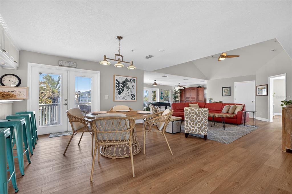 An open-concept living and dining area features wood-look flooring, a red sofa, and wicker chairs — 1902 ARROWHEAD DRIVE NE, ST PETERSBURG, FL