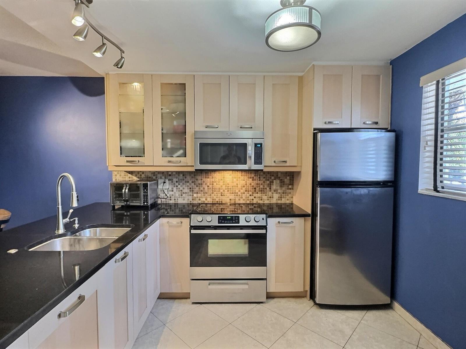 A kitchen features light wood cabinets, stainless steel appliances, black countertops, and blue walls — 3150 Holiday Springs Boulevard # 204, Margate FL 33063, MARGATE, FL