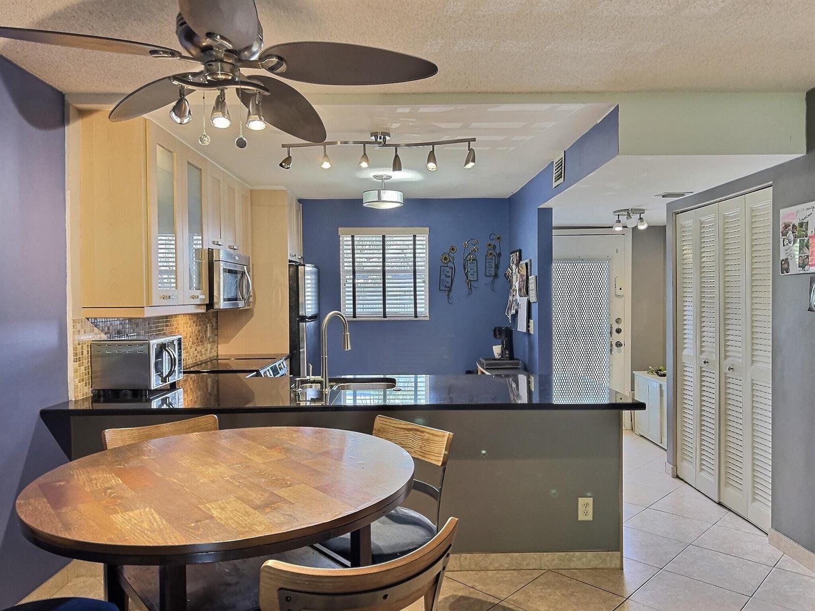 A kitchen with light wood cabinets, black countertops, and a round dining table — 3150 Holiday Springs Boulevard # 204, Margate FL 33063, MARGATE, FL