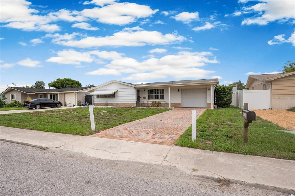 A single-story house with white siding, a brick driveway, and an attached garage — 3410 COLUMBUS DRIVE, HOLIDAY, FL