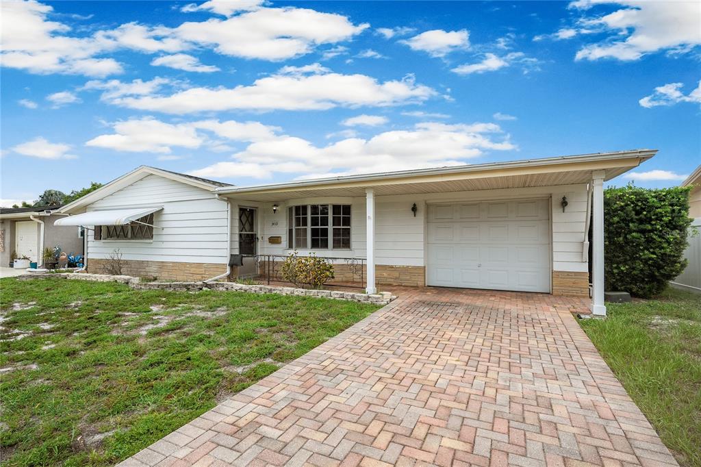 A single-story white house features a brick-paved driveway, a carport, and a stone-accented exterior — 3410 COLUMBUS DRIVE, HOLIDAY, FL
