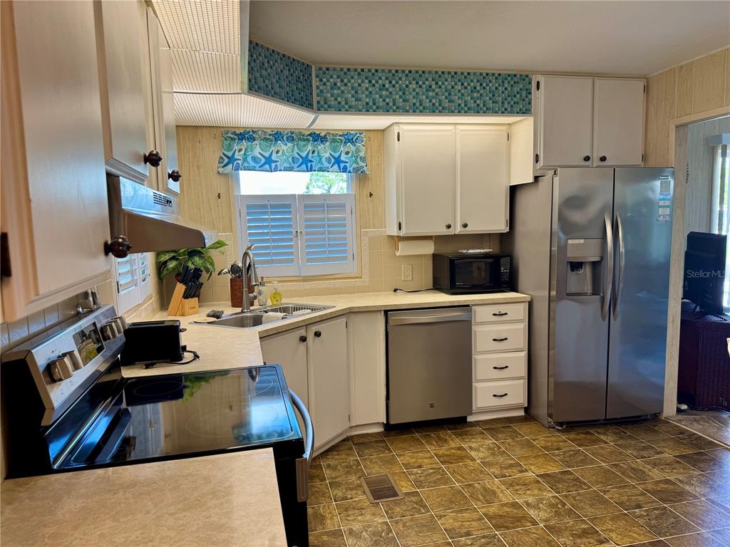 A kitchen features white cabinets, stainless steel appliances, a tiled backsplash, and patterned flooring — 203 ESTRADA, NORTH PORT, FL