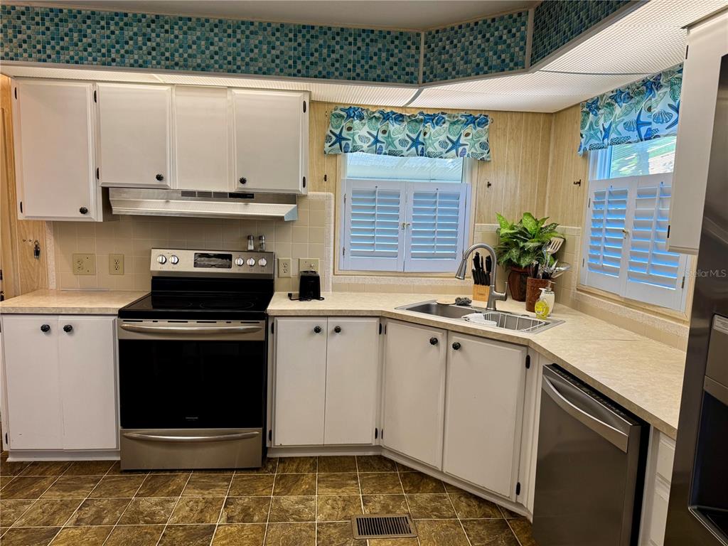 A kitchen features white cabinets, stainless steel appliances, a tiled backsplash, and a corner sink — 203 ESTRADA, NORTH PORT, FL