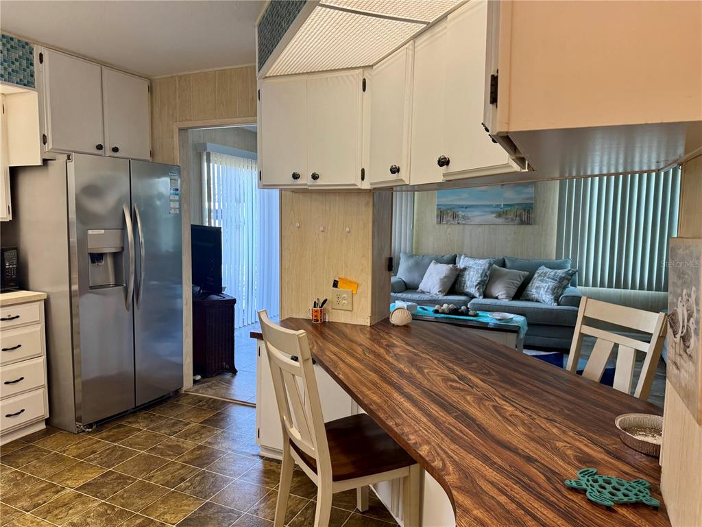 A kitchen with white cabinets and a wood-grain breakfast bar overlooks a living area — 203 ESTRADA, NORTH PORT, FL