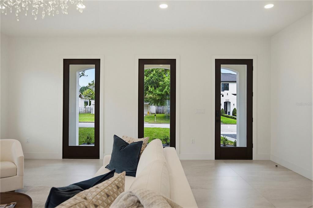 A bright living room features three tall dark-framed glass doors overlooking a suburban street — 2430 CHANTILLY AVENUE, WINTER PARK, FL