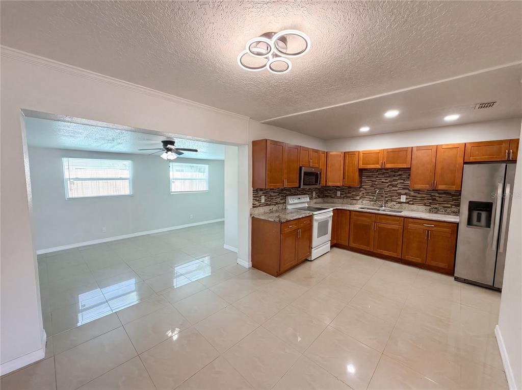 A kitchen with wood cabinets and tile flooring opens into a living area with windows — 15525 BEDFORD CIRCLE E, CLEARWATER, FL