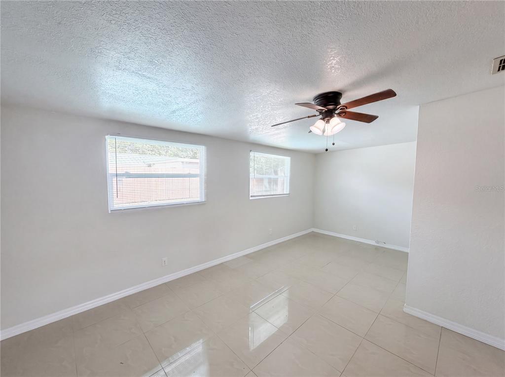 An empty room with light-colored tile flooring, white walls, two windows, and a ceiling fan — 15525 BEDFORD CIRCLE E, CLEARWATER, FL